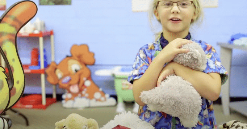 Young girl in scrubs playing with stuffed animals